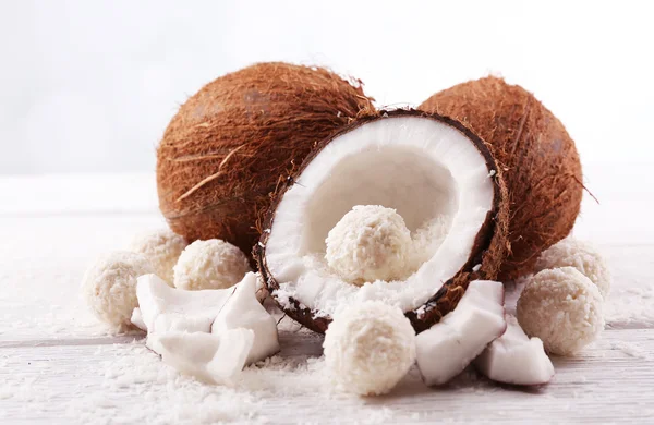 Candies in coconut flakes and fresh coconut on  light wooden background