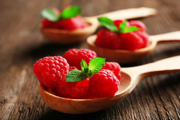 Fresh red raspberries in spoons on wooden table, closeup — Stock Photo, Image