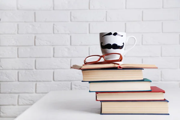 Vintage boeken en cup met snor op houten tafel op bakstenen muur achtergrond — Stockfoto