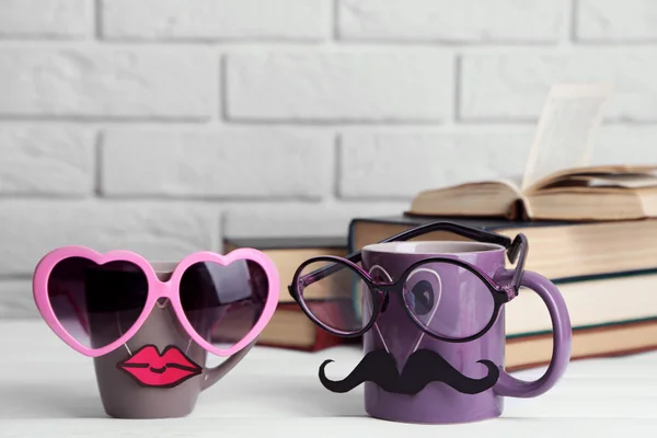 Vintage books and cup with mustache and lips on wooden table on brick wall background — Stock Photo, Image