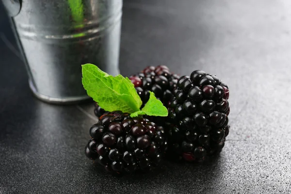 Ripe blackberries with green leaves on dark surface, closeup — Stock Photo, Image