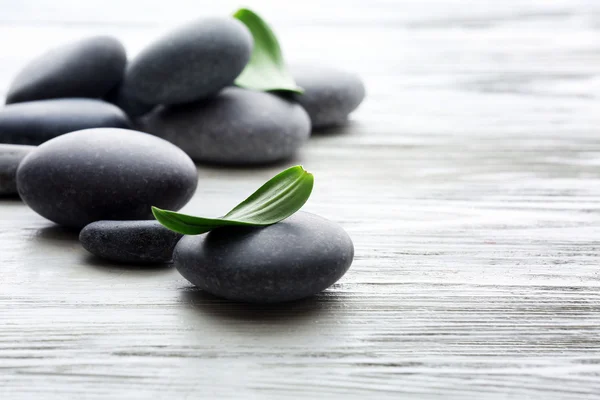 Spa stones with green leaves on wooden background — Stock Photo, Image