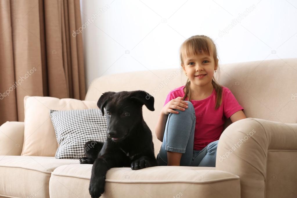 girl with puppy on sofa at home