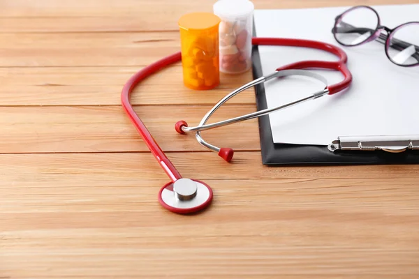 Medyczny stetoskop ze schowka i tabletki na drewnianym stole z bliska — Zdjęcie stockowe