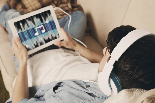 Pohledný mladý muž ležel na pohovce a poslouchá hudbu v místnosti — Stock fotografie