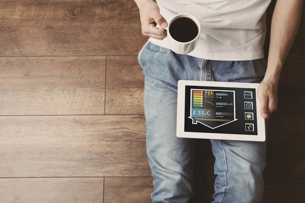 Young man sitting on floor with tablet and cup of coffee in room — Stock Photo, Image