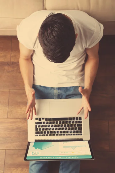 Молодой человек сидит на полу с ноутбуком в комнате — стоковое фото
