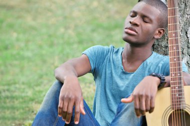 Afro-Amerikan yakışıklı parkta oturup gitar ile