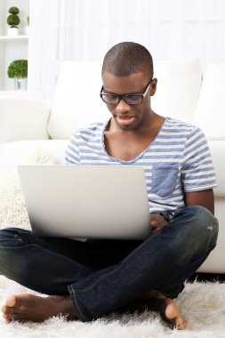 Yakışıklı Afrikalı-Amerikalı adam odada halı üstünde laptop ile oturuyor