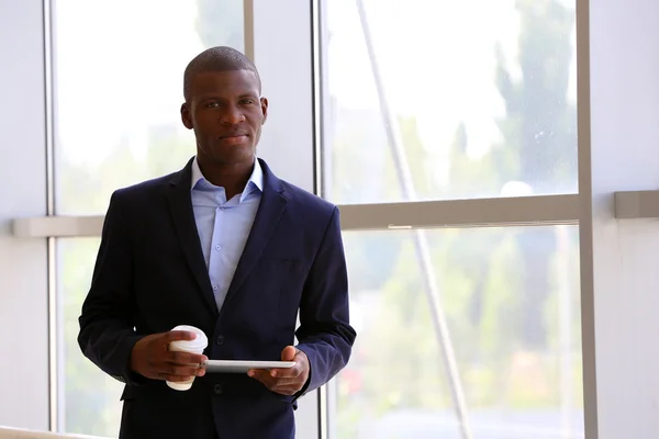 Bonito empresário afro-americano com tablet e xícara de café no escritório — Fotografia de Stock