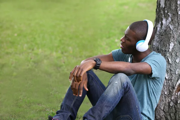 Bonito afro-americano com fones de ouvido sentado no parque — Fotografia de Stock