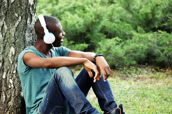 Bello uomo afroamericano con le cuffie seduto nel parco — Foto Stock