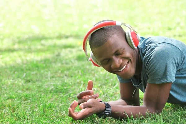 Bello uomo afroamericano con le cuffie sdraiato su erba verde — Foto Stock