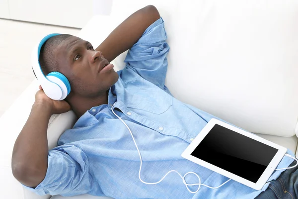 Hombre afroamericano guapo con auriculares y tableta acostado en el sofá de cerca —  Fotos de Stock