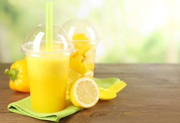 Salade de légumes et fruits jaunes et boisson fraîche saine dans des tasses en plastique sur table en bois, sur fond lumineux. Concept de régime coloré — Photo