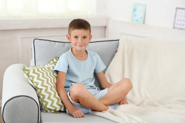 Niño sentado en el sofá, en el fondo interior de casa — Foto de Stock