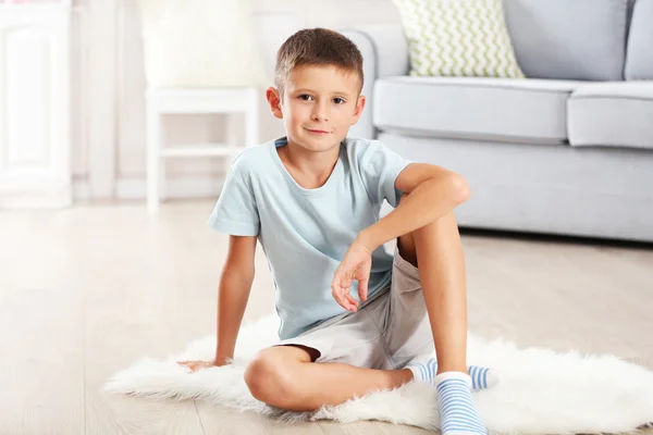 Mały chłopiec siedzi na dywanie, na tle wnętrz domu — Zdjęcie stockowe