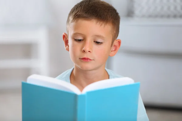 Liten pojke med bok sitter på mattan, på hem inredning bakgrund — Stockfoto