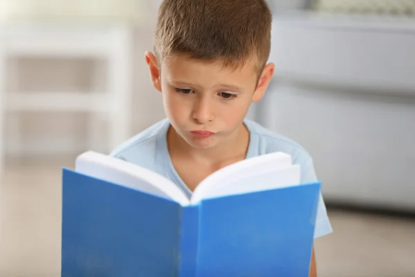 ホーム インテリアの背景に、カーペットの上に座って本を持った少年 — ストック写真