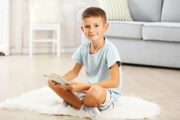 Mały chłopiec cyfrowy tablicowy siedzi na dywanie, na tle wnętrz domu — Zdjęcie stockowe