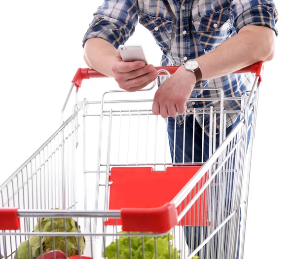 Young man holding mobile phone and shopping cart isolated on white — Stock Photo, Image