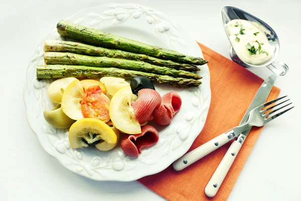 Ψητό Σπαράγγια και το γευστικό πολύχρωμα ζυμαρικά με λαχανικά στο πιάτο σε ξύλινο τραπέζι φόντο — Φωτογραφία Αρχείου