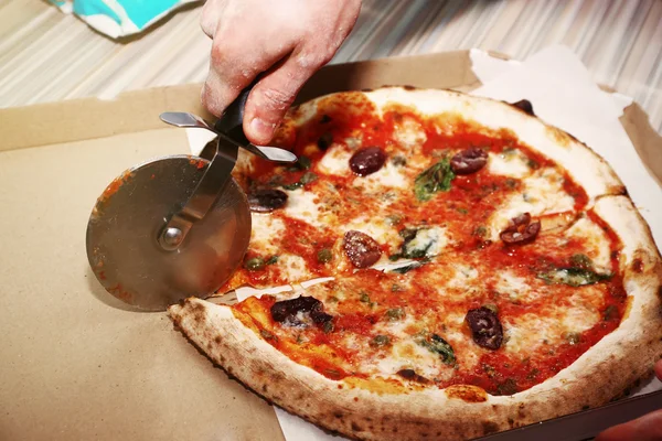 Macho mão corte pizza com lâmina de pizza na caixa, close-up — Fotografia de Stock