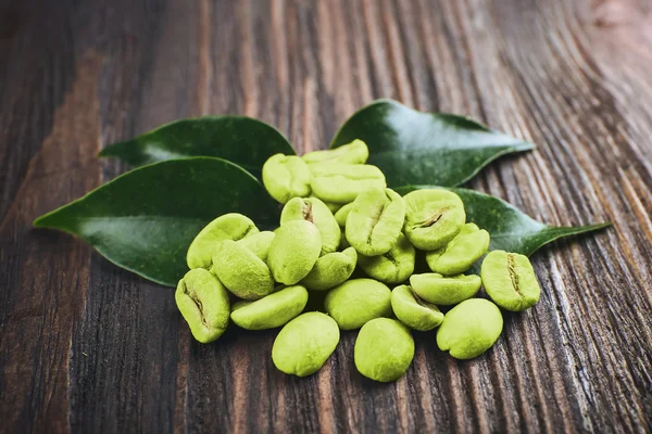 Chicchi di caffè verde con foglie su sfondo di legno — Foto Stock