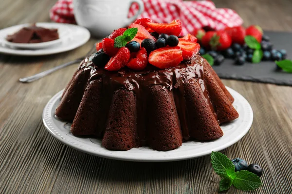 Delicioso bolo de chocolate com bagas em prato na mesa, close-up — Fotografia de Stock