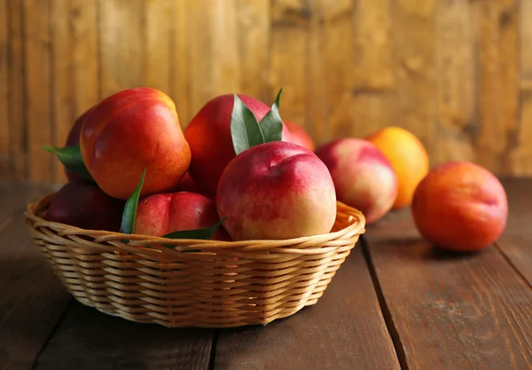 Fresh peaches in wicker basket on wooden background — Stock Photo, Image