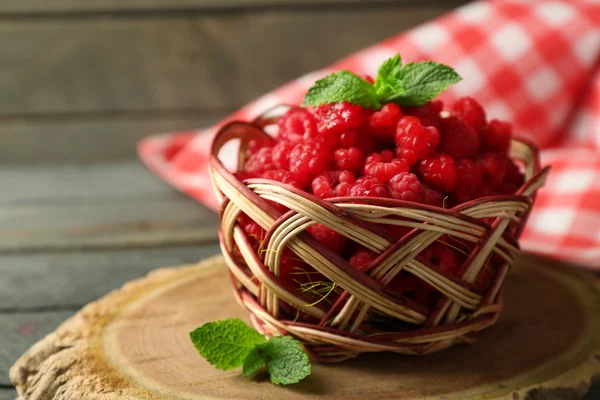 Sweet raspberries in wicker basket on wooden  background