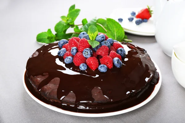 Delicioso bolo de chocolate com bagas de verão em toalha de mesa cinza, close-up — Fotografia de Stock