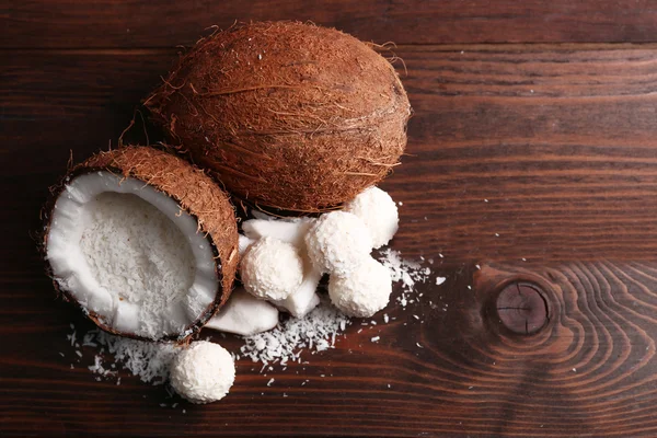 Bonbons in Kokosflocken und frischen Kokosnüssen auf dunklem Holzhintergrund — Stockfoto