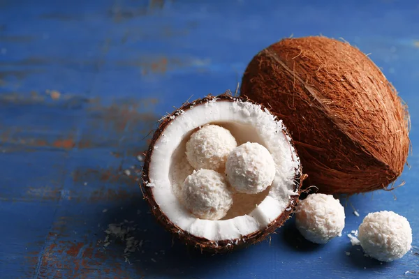 Bonbons in Kokosflocken und frischen Kokosnüssen auf farbigem Holzhintergrund — Stockfoto