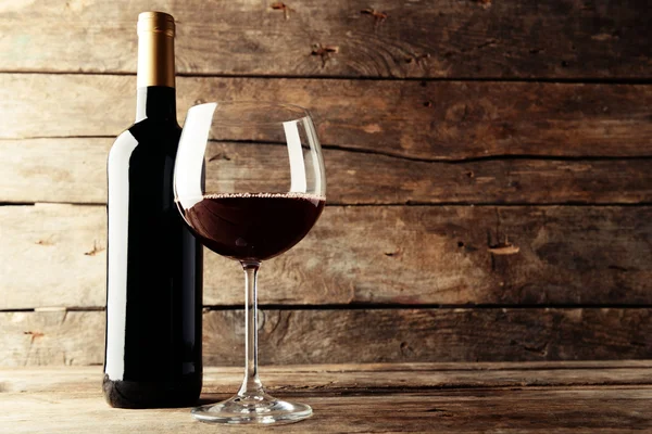 Una botella de vino tinto y una copa sobre una mesa de madera — Foto de Stock