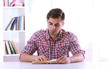 Genç adam odada masasında kitap okumak