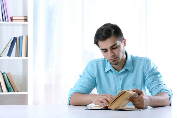 Jeune homme lisant un livre à table dans la chambre — Photo
