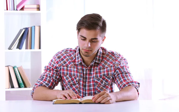 Mladý muž čtení knih u stolu v pokoji — Stock fotografie