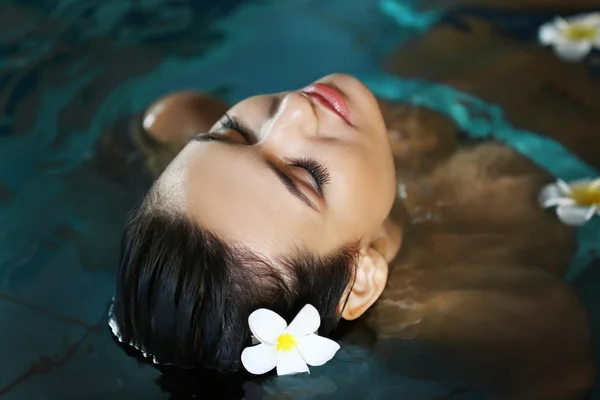 Mooie jonge vrouw met bloemen bij zwembad — Stockfoto