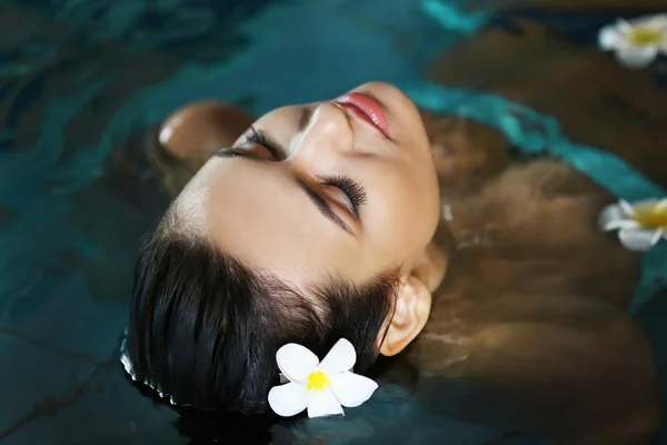 Mulher bonita com flores na piscina — Fotografia de Stock