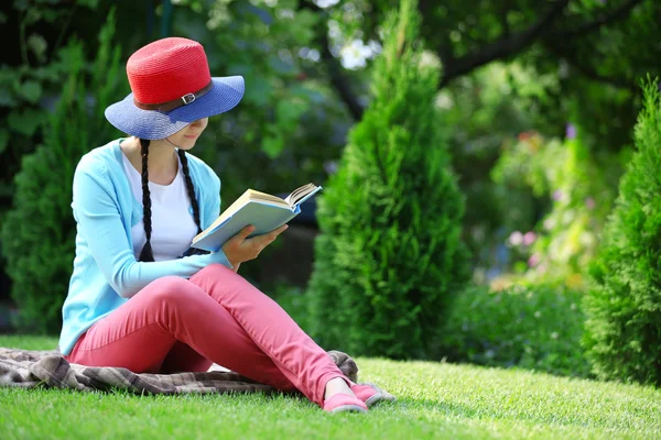 Young woman with book sitting on green grass outdoors — Stock Photo, Image