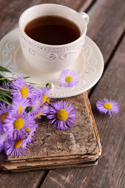 Libro viejo con hermosas flores y taza de té en la mesa de madera de cerca — Foto de Stock