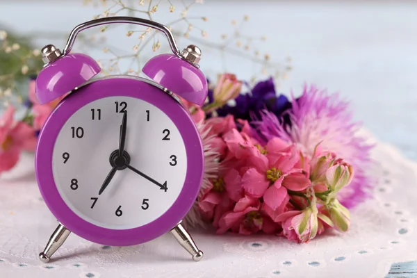 Liten väckarklocka med vackra blommor på bordet på nära håll — Stockfoto