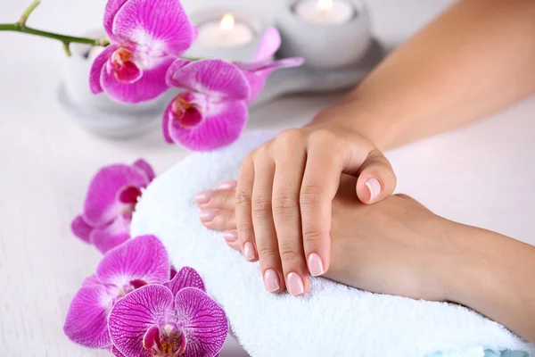 Mãos da mulher com manicure francês e flores do orchid na tabela de madeira close-up — Fotografia de Stock