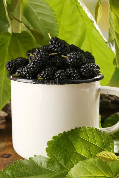 Mulberries maduras em caneca com folhas verdes na mesa close-up — Fotografia de Stock