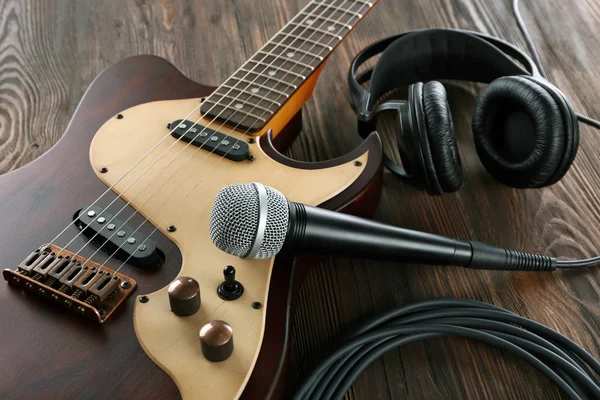 Elektrická kytara s mikrofonem a sluchátky na dřevěný stůl zblízka — Stock fotografie