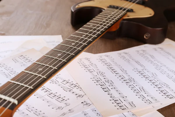 Chitarra elettrica con note musicali sul tavolo di legno da vicino — Foto Stock