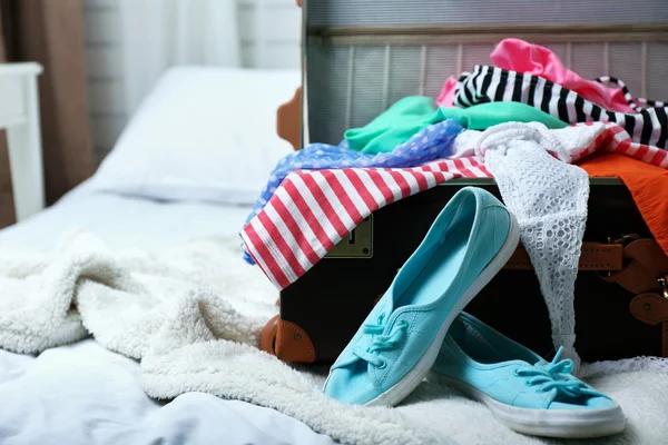 Suitcase with clothing on bed in room — Stock Photo, Image