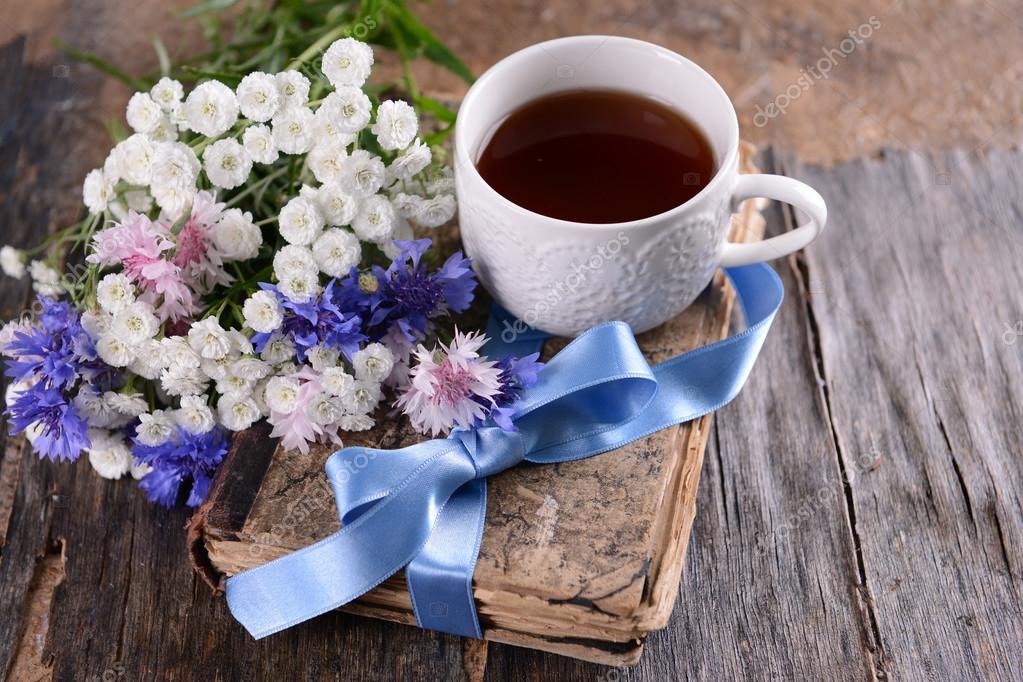Old book with beautiful flowers and cup of tea on wooden