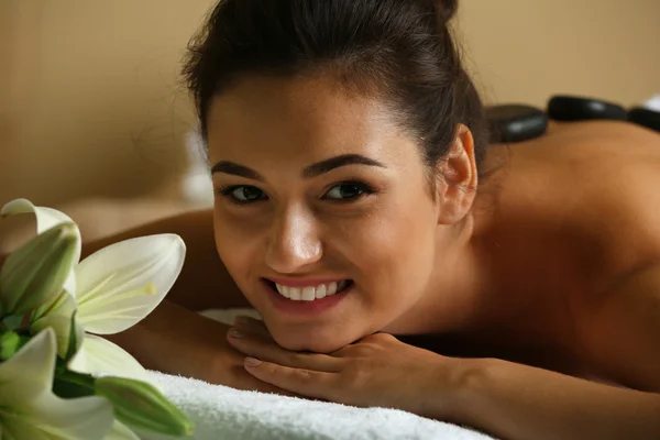 Mujer joven con piedras de spa en la espalda en la mesa de masaje en el salón de spa de belleza —  Fotos de Stock